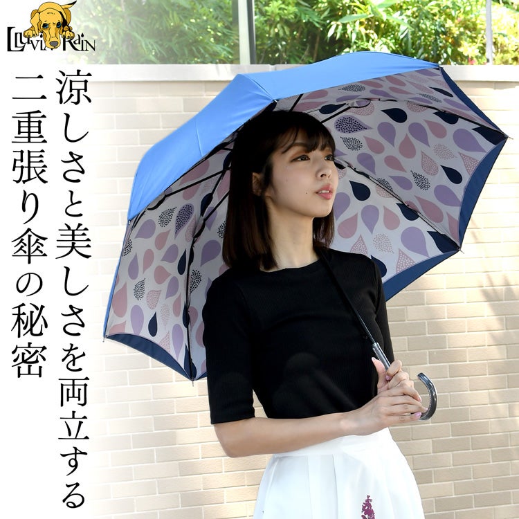 ネイビーの外生地と、内側に広がる明るいティアドロップ柄を組み合わせた、ルビアレインの二重張り晴雨兼用長傘を軽やかに差す大人の女性