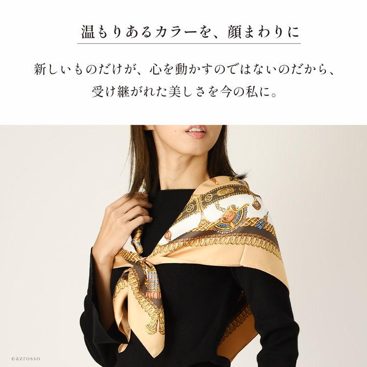 黒トップスの肩にブラウンの馬具柄シルクスカーフを広げ、胸元でまとめた着用例。金色とアイボリーの柄が見える前姿