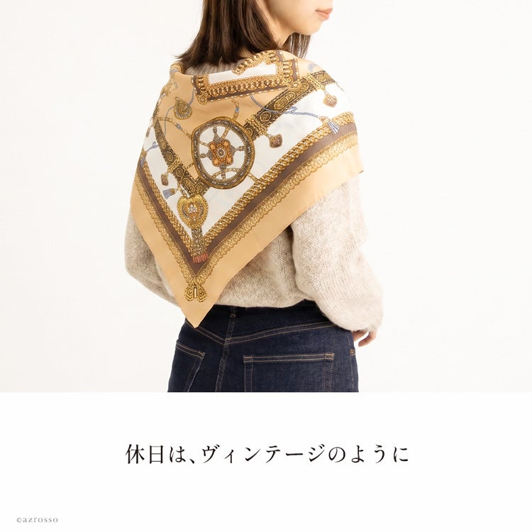 生成りのニットとデニムに、馬具柄シルクスカーフを三角形に肩掛けした休日コーデ。背中に広がるブラウンと金色の柄