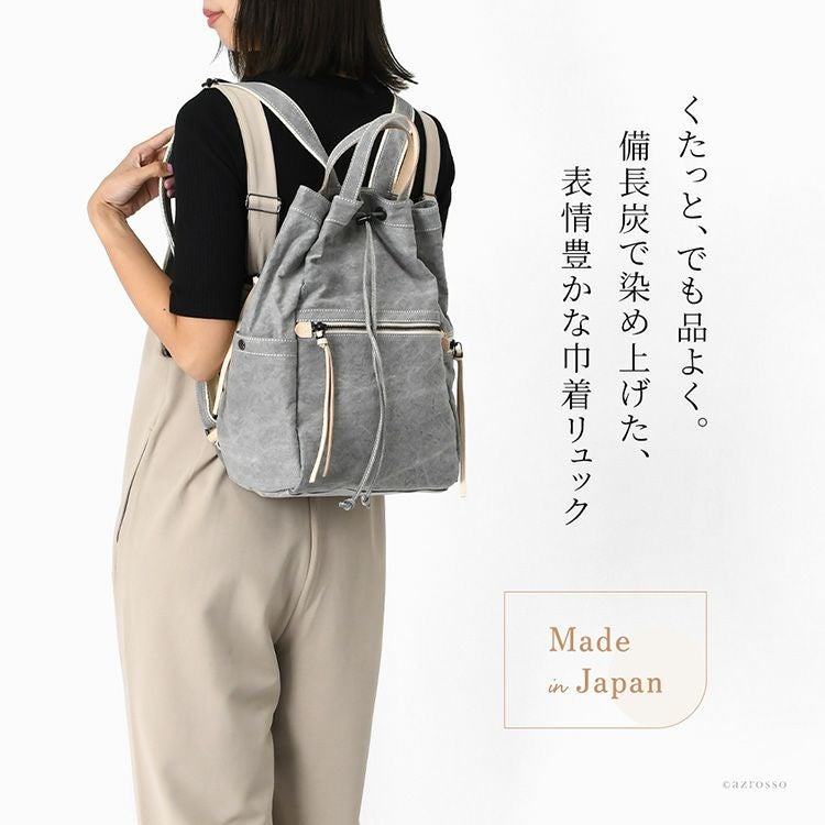 軽量で畳める日本製巾着リュックを背負う女性モデル。帆布素材で大容量、A4収納可。背面ファスナー直結やサイドポケットで機能的なレディースリュック
