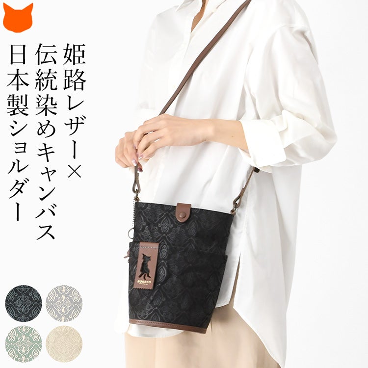 上品なダマスク柄にさりげない猫モチーフを施した日本製キャンバスショルダーバッグを使用する女性モデル。帆布×姫路レザーを使用した縦型軽量ミニバッグ。