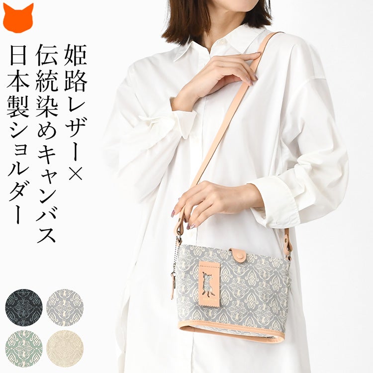 上品なダマスク柄にさりげない猫モチーフを施した日本製キャンバスミニショルダーバッグを使用する女性モデル。帆布×姫路レザーを使用した横長軽量ミニバッグ。