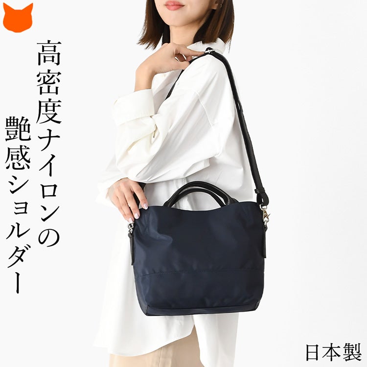 高密度ツイルナイロンとシボ牛革を組み合わせた2WAYショルダーバッグを肩掛けして微笑む女性。斜め掛け対応、軽くて大容量の上品ナイロンバッグ