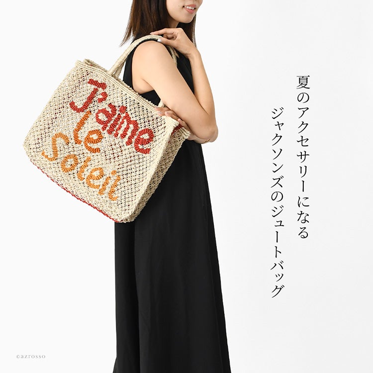夏のアクセサリーになるジャクソンズのジュートバッグ。ナチュラルなジュート素材に鮮やかなカラーが映え、リゾートのような抜け感と高揚感を添えてくれる大容量トートバッグを肩掛けして歩く女性