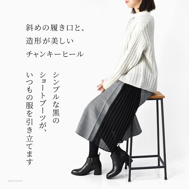 斜めの履き口と造形的な太ヒールが印象的な、黒の本革アンクルブーツを着用した女性モデル